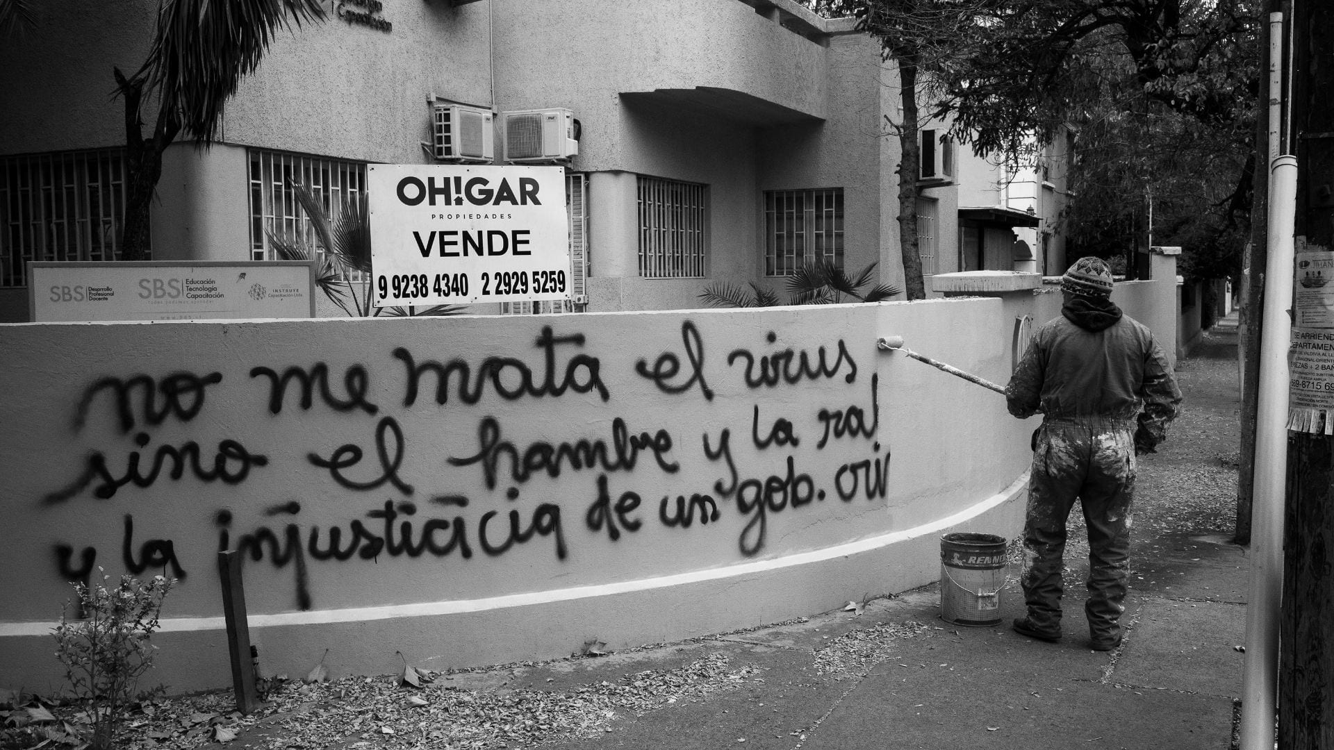 worker painting over graffiti that says: the virus is not killing me but hunger and injustice of a criminal government are