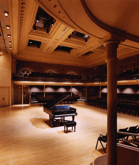 A size view of an empty Lowell Lecture Hall other than a lone piano center stage
