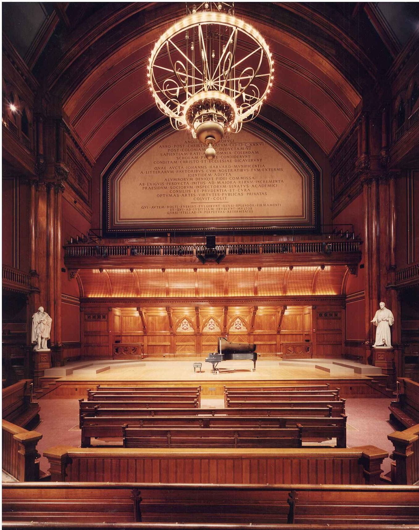 A view of Sanders Theatre's stage from the center audience perspective. A large chandelier hangs over piano centered on the stage area